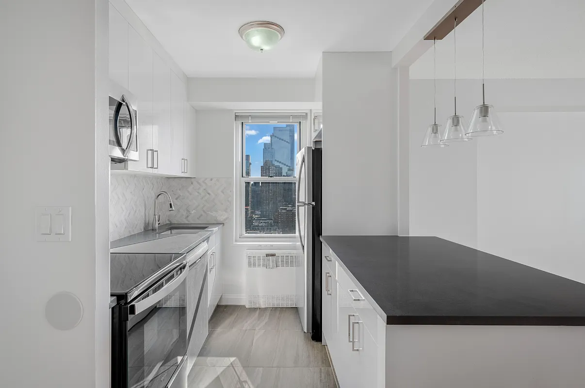 Unit 26J - completed galley kitchen with white cabinetry, dark quartz counter, and skyline view