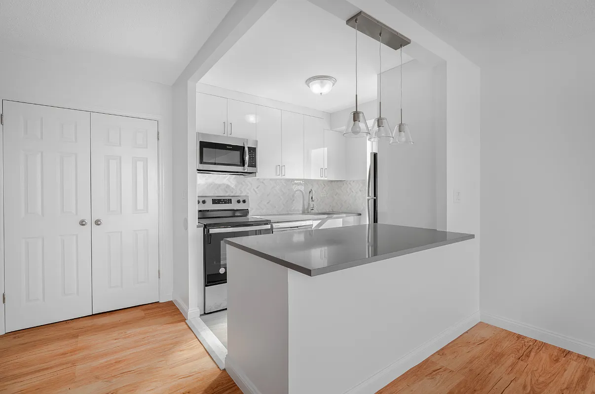 Unit 37B - completed kitchen with white shaker cabinets, herringbone marble backsplash, and quartz peninsula